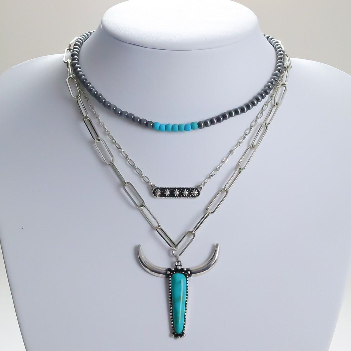 Layered silver-tone necklaces with a turquoise-colored bull-head pendant displayed on a bust
